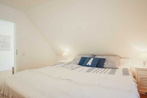 A bedroom with a bed, two bedside tables, and a door. - Holiday home with 3 bedrooms (Ostseebad Prerow)