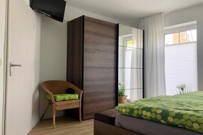 A bedroom with a bed, a chair, a wardrobe, and a window with curtains. - Park Residence at Hafen 11 - "MeerZeit" (Seeheilbad Zingst)