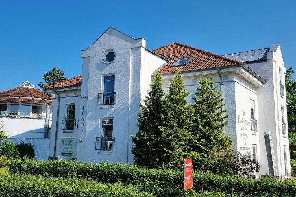 A white building with a red-tiled roof, a circular window, and a sign indicating a restaurant.