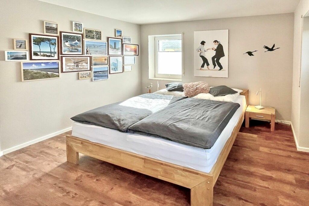 A bedroom with a wooden bed, a nightstand, a wall with framed pictures, and a window.