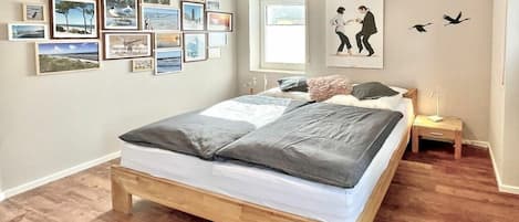 A bedroom with a wooden bed, a nightstand, a wall with framed pictures, and a window.
