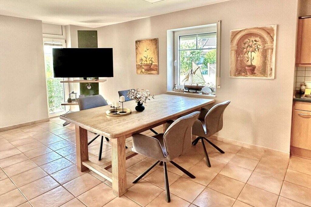 A dining area with a wooden table, four chairs, a flat-screen TV mounted on the wall, and artwork on the walls.