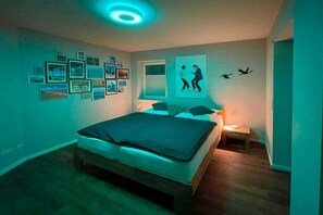 Une chambre à coucher avec un lit, des tableaux accrochés au mur, une fenêtre et un luminaire au plafond.