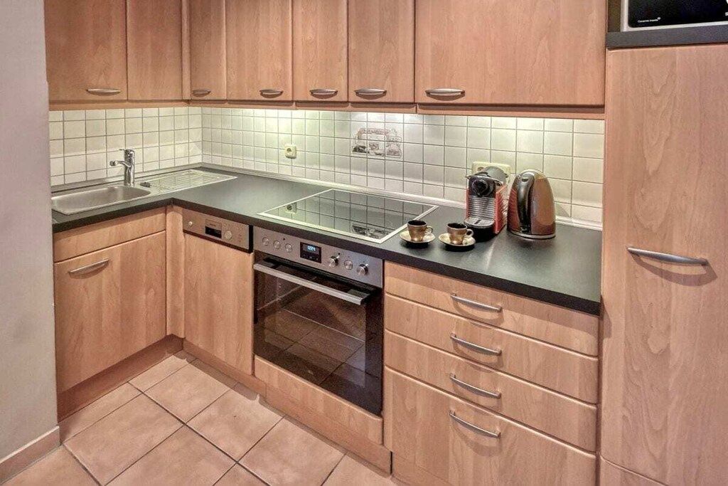 A compact kitchen with wooden cabinets, a built-in oven, a sink, and a coffee maker.