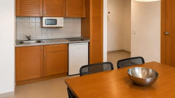 A compact kitchen with wooden cabinets, a microwave, a sink, and a dishwasher. There is a dining table with chairs and a metal bowl on it.