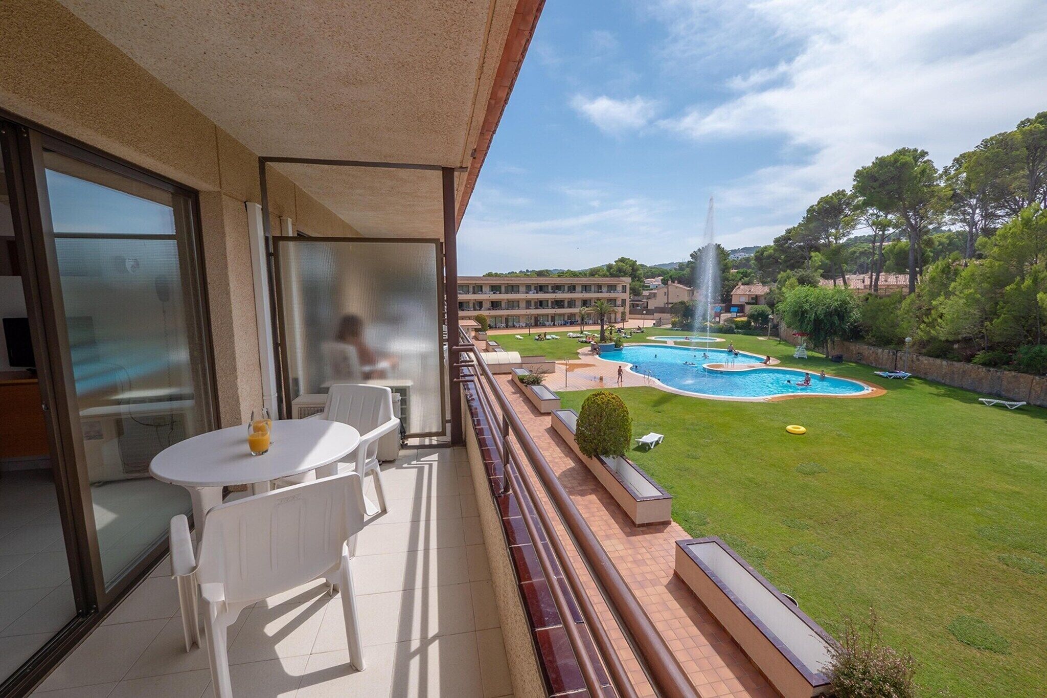 Un balcon avec une table et des chaises, donnant sur une piscine et une pelouse bien entretenue.