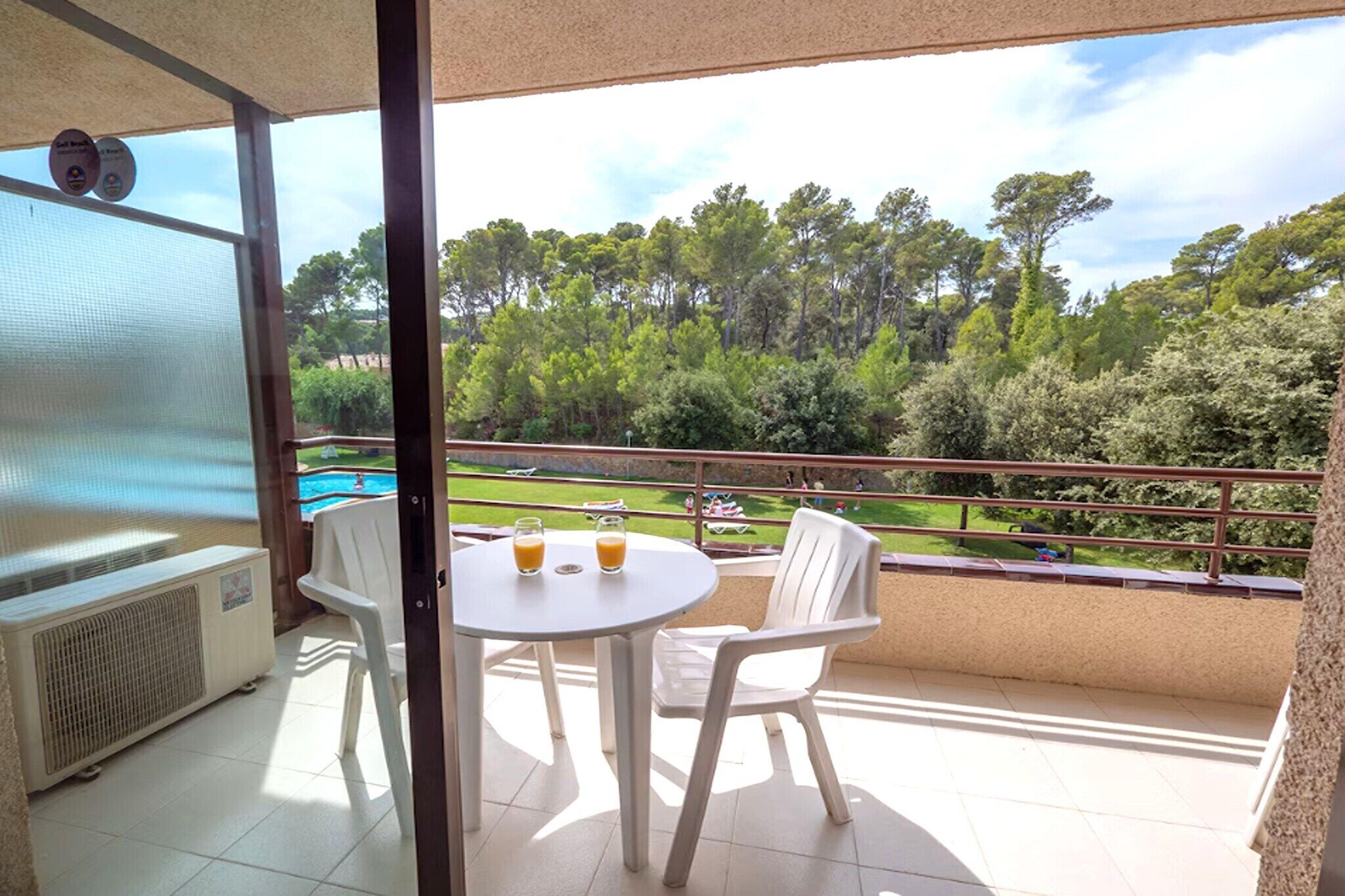 A balcony with a pool, white chairs, and a table with drinks.