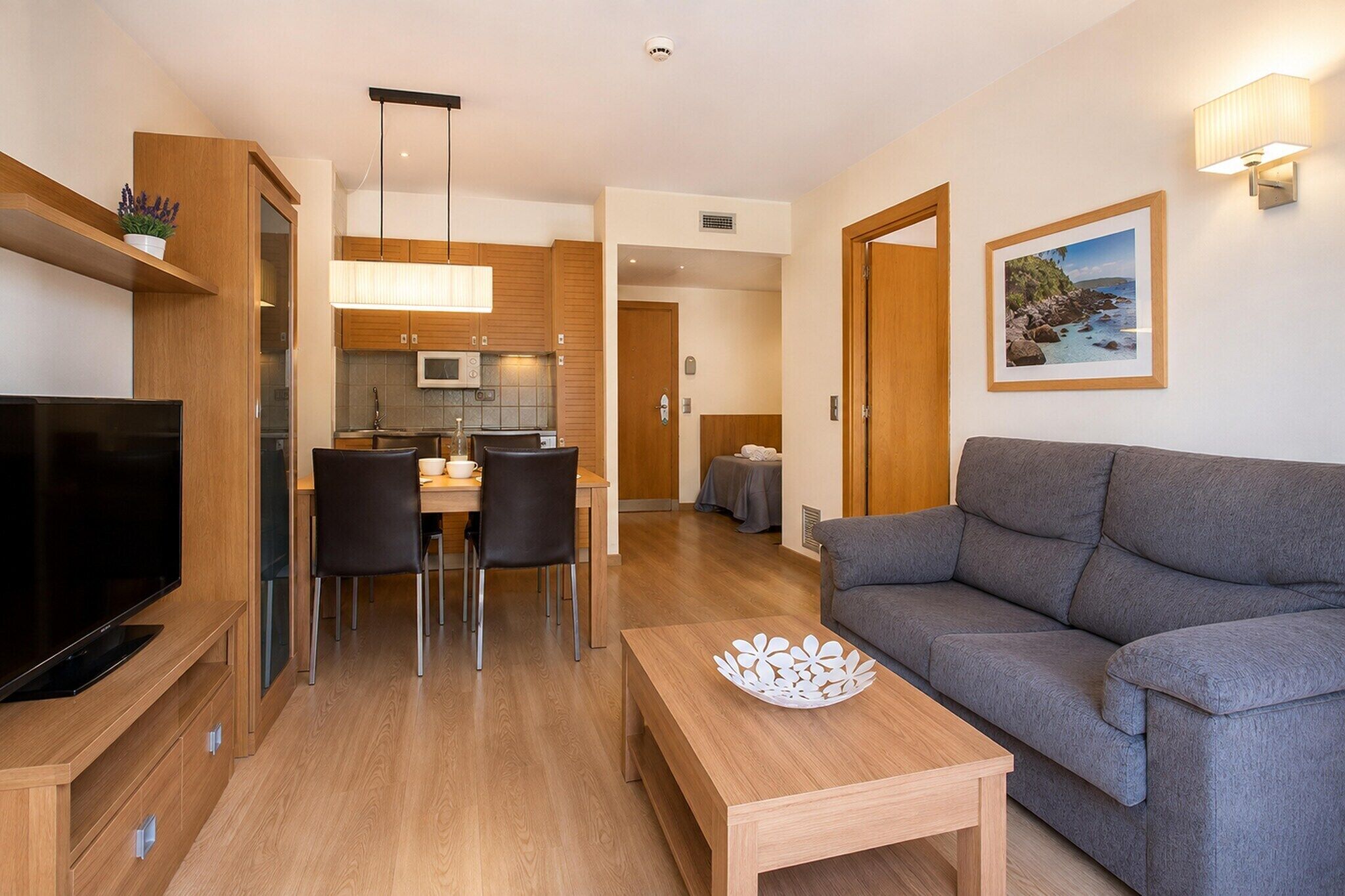 Una sala moderna con un televisor de pantalla plana, un sofá gris y una zona de comedor con sillas y una mesa.