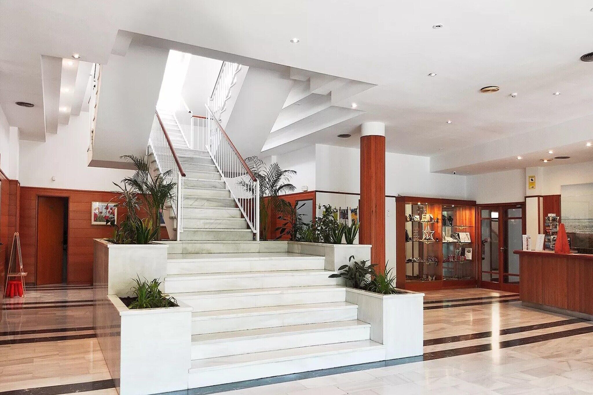Un hall d’hôtel moderne avec un escalier central, un comptoir d’accueil et une présentation d’objets.