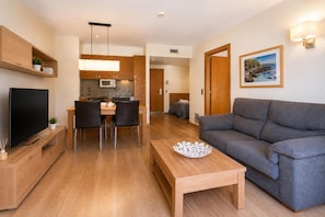 Een moderne woonkamer met een grijze bank, een houten salontafel en een flatscreen televisie.