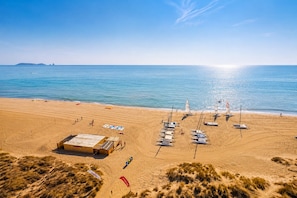 Een strand met een zandvlakte, een klein gebouw en verschillende zeilboten.