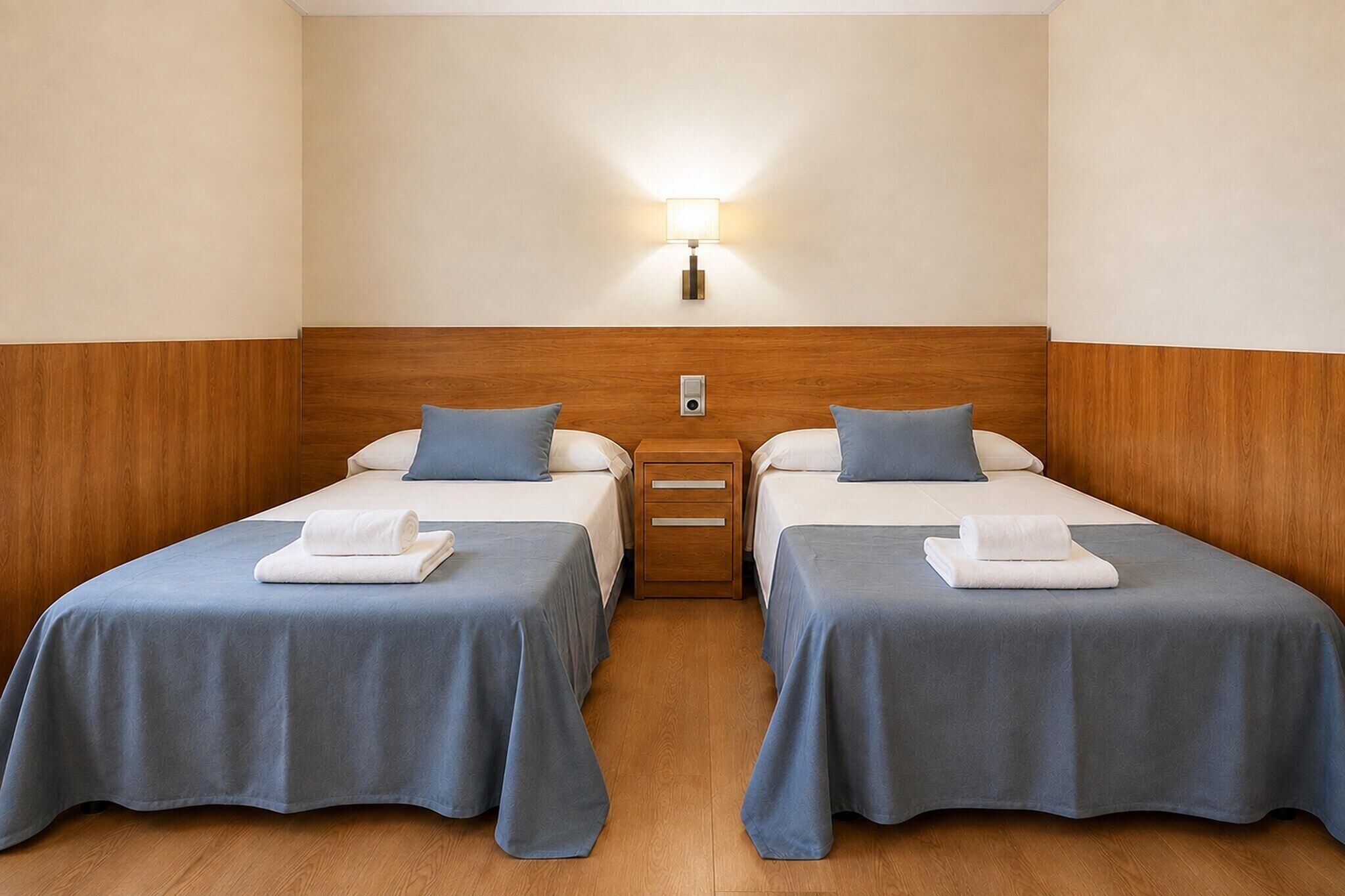 Een hotelkamer met twee enkele bedden, elk met een kussen en een opgerolde handdoek.