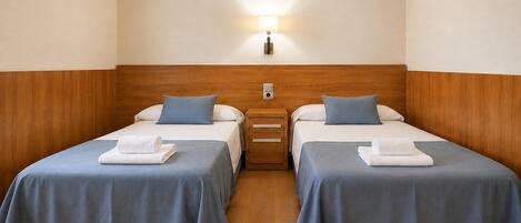Habitación de hotel con dos camas individuales, cada una con una almohada y una toalla enrollada.