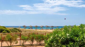 Een strand met parasols, een hek en begroeiing.
