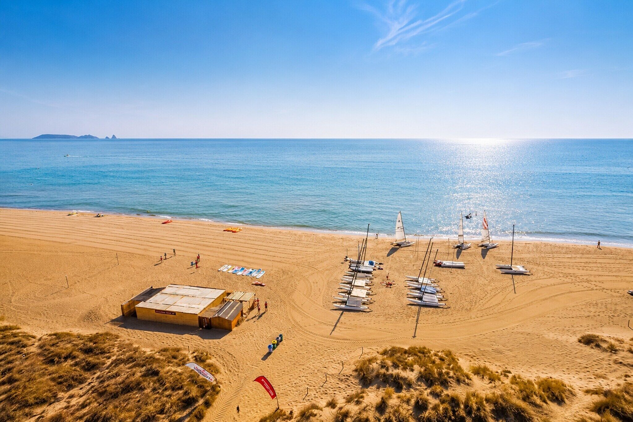 Een strand met een zandvlakte, een klein gebouw en verschillende zeilboten.