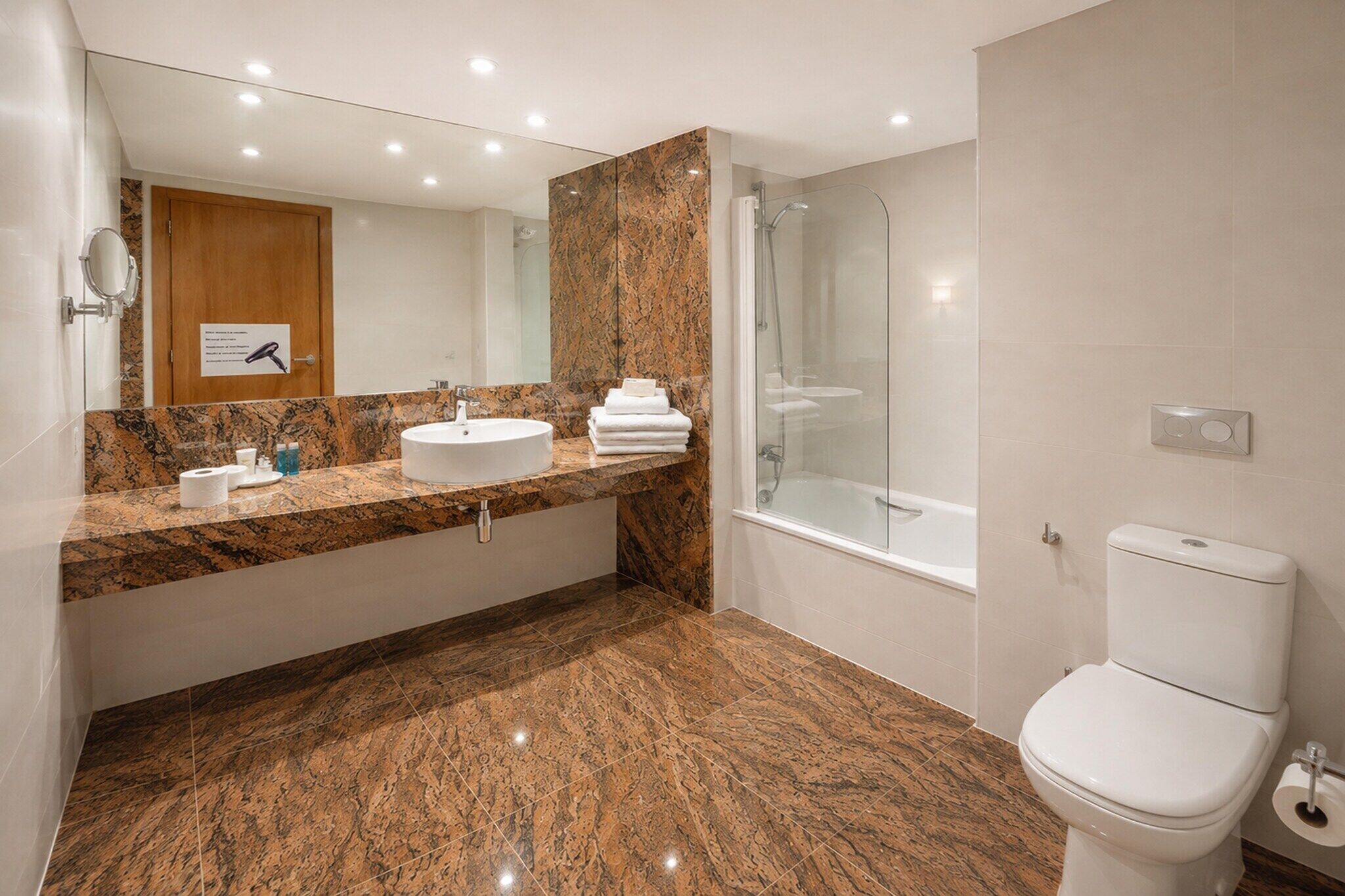 Een moderne badkamer met een marmeren aanrechtblad, een wastafel, een toilet en een douchecabine met glazen wanden.