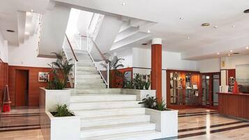 Een moderne hotellobby met een centrale trap, een receptiebalie en een presentatie van objecten.