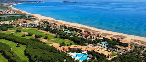 An aerial view of a coastal resort with a beach, golf course, and swimming pool.