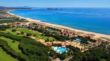 An aerial view of a coastal resort with a beach, golf course, and swimming pool.