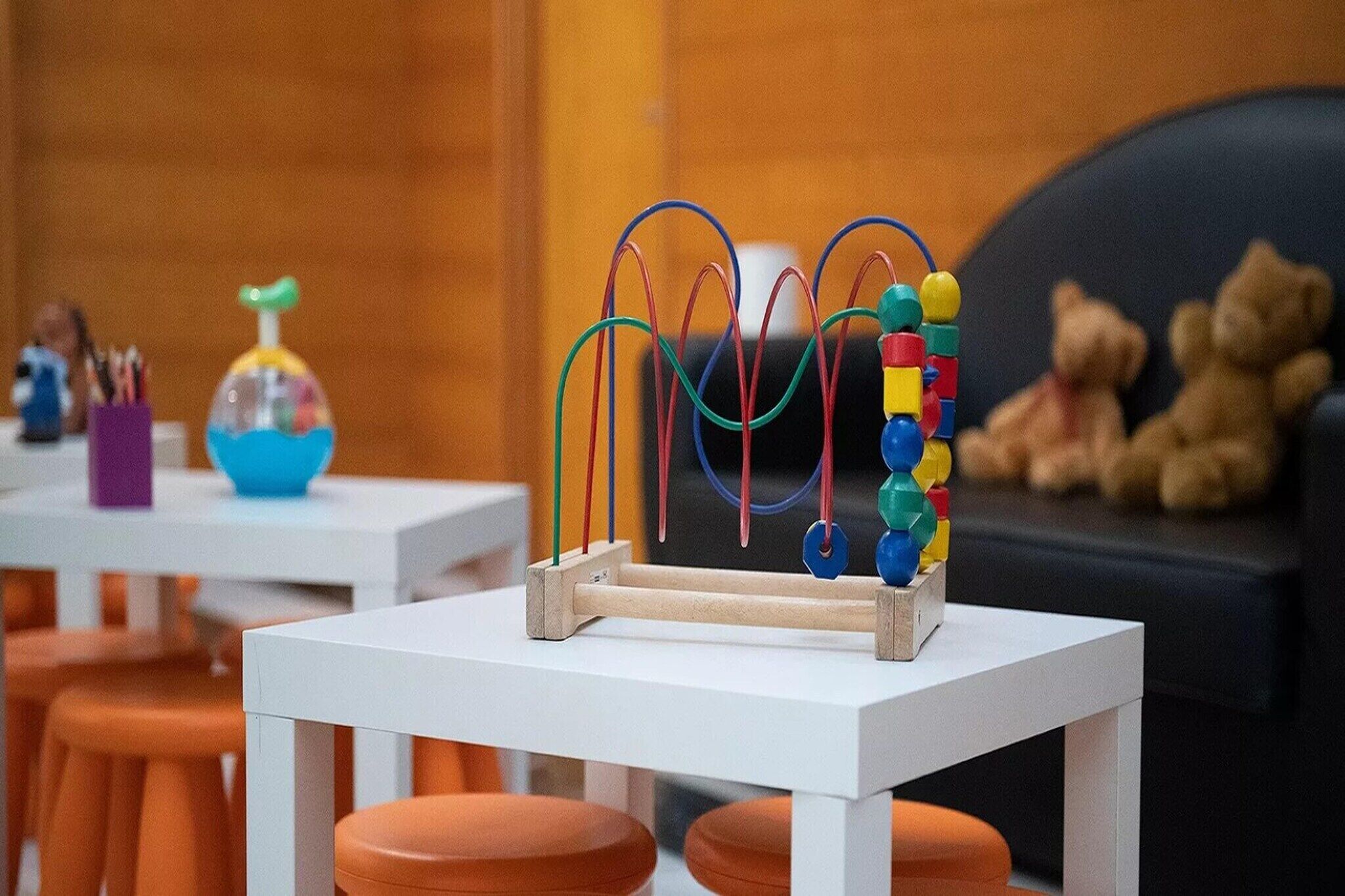 Un espace de jeux pour enfants avec une table en bois, des perles colorées et un jouet dont le sommet est vert.