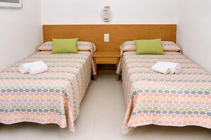 Een tweepersoonskamer met twee bedden, elk met een bedovertrek met dessin en een groene kussen.