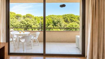 Een kamer met een schuifglazen deur die leidt naar een buitenbalkon met uitzicht op een groen landschap.