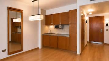 Een moderne keuken met houten kastjes, een magnetron en een spoelbak. Er is een gang met een deur en een lamp.