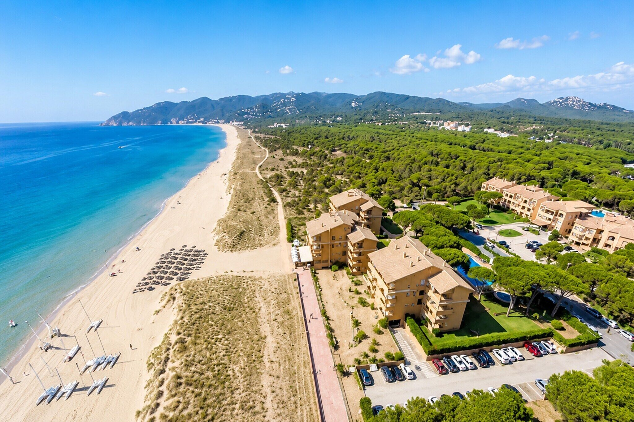 A coastal resort with a beach, multiple-story buildings, and a parking area.