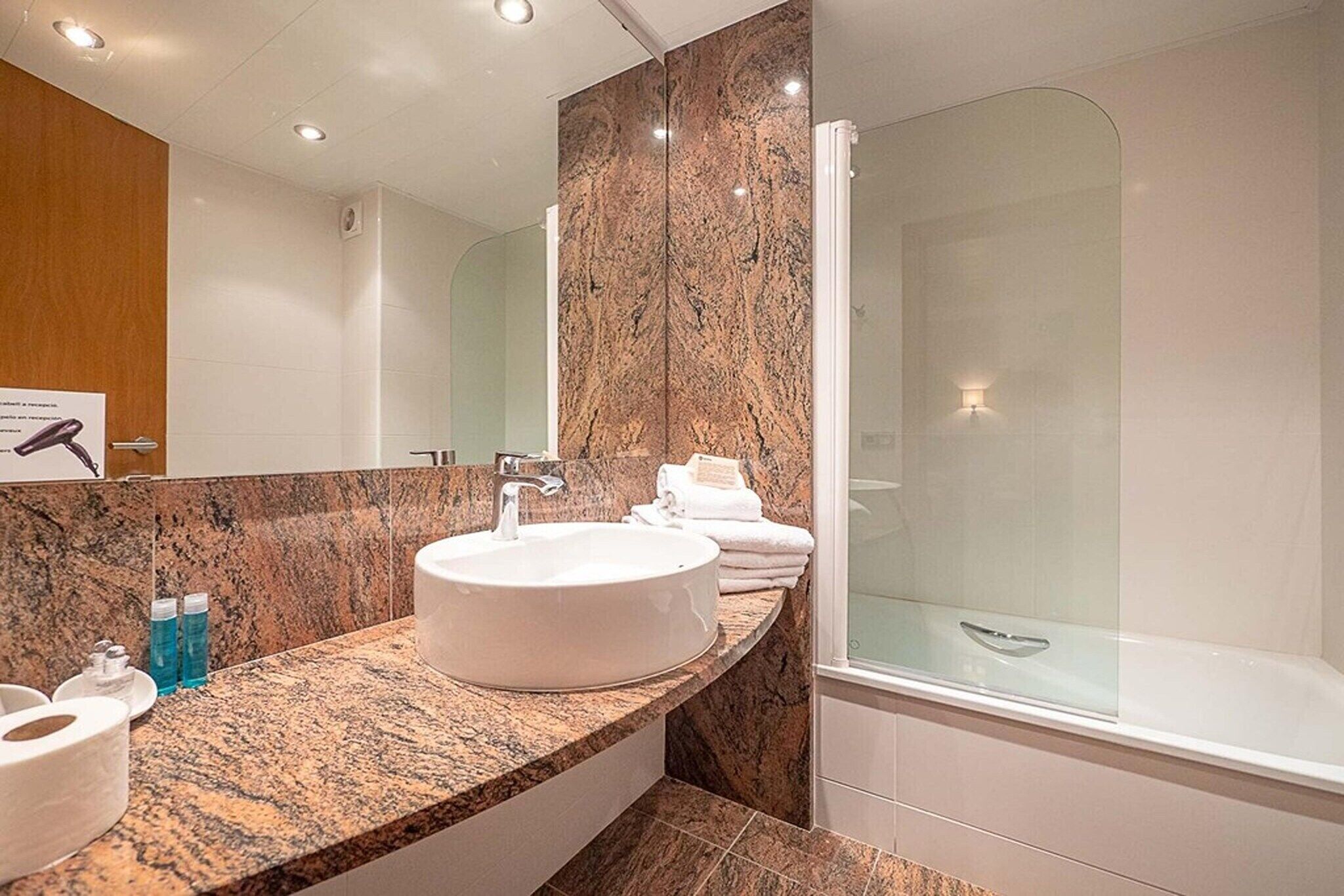 Een moderne badkamer met een rond wastafel, een douchecabine met glazen wanden en een marmeren aanrechtblad.