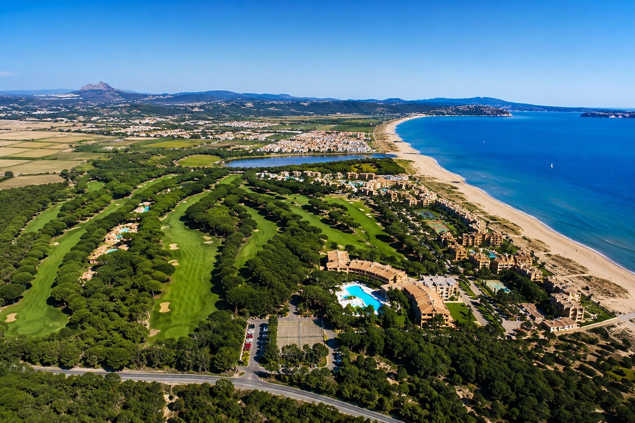 An aerial view of a coastal resort with a golf course, a swimming pool, and a beach.
