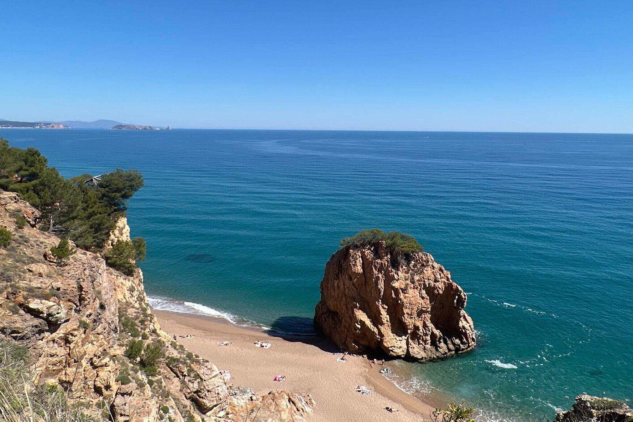 A coastal landscape with a rocky cliff, a sandy beach, and a clear blue sea.