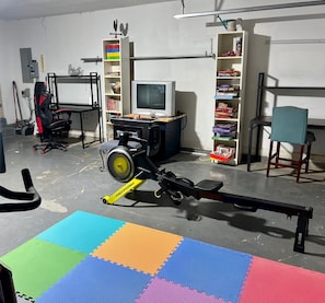 A room with a stationary bike, a television, and a bookshelf.