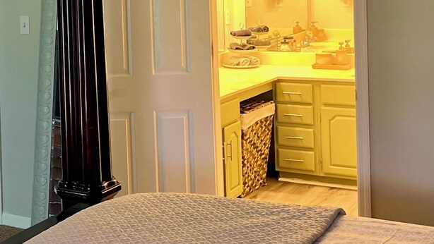 Une chambre à coucher comprenant un lit, une porte donnant sur une salle de bain et un petit coin cuisine avec un évier et des placards.