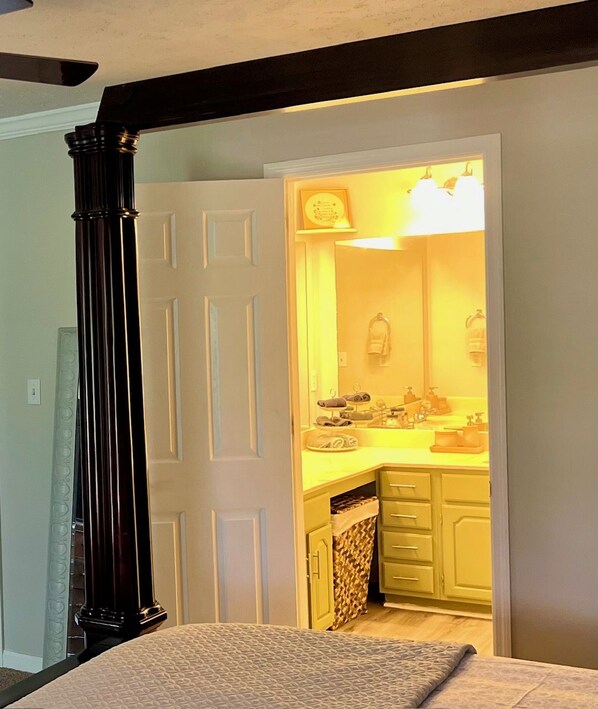 A bedroom with a bed, a door leading to a bathroom, and a small kitchen area with a sink and cabinets.