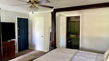 Une chambre à coucher comprenant un lit, un ventilateur de plafond, une commode et une porte donnant sur une salle de bain.
