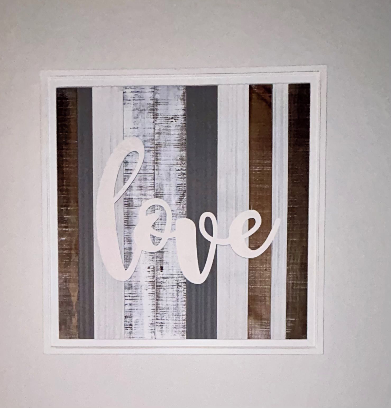 A framed artwork with the word 'love' in a cursive font, set against a background of vertical stripes in varying shades of gray and brown.