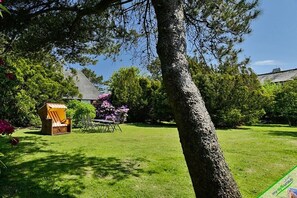 A grassy outdoor area with a wooden chair and table, surrounded by trees and shrubs. - Country house East Coast (Keitum)