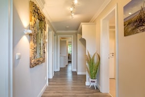 A hallway with a wooden floor, a decorative mirror, wall sconces, and a potted plant. - Country house East Coast (Keitum)