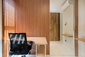 A modern office space with a wooden panel wall, a black office chair, a wooden desk, and a white door. - Evita Villa by Betterplace (Canggu)