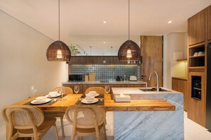 A modern kitchen with a central island, wooden cabinets, and a built-in microwave. - Evita Villa by Betterplace (Canggu)