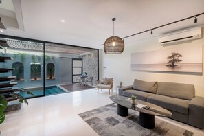 A modern living room with a grey sofa, a coffee table, and a hanging light fixture. - Evita Villa by Betterplace (Canggu)
