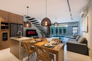 A modern kitchen with a built-in refrigerator, a dining area with a table set for four, and a living area with a sofa and a TV displaying the Netflix logo. - Evita Villa by Betterplace (Canggu)