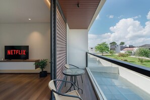 Ein modernes Wohnzimmer mit einem Flachbildfernseher, der 'NETFLIX' anzeigt, einem Holzboden, einer Topfpflanze, einem Glastrennstreifen und Blick auf eine Wohngegend.