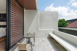 A balcony with a table and two chairs, a white wall, and a view of a red-tiled roof and greenery. - Evita Villa by Betterplace (Canggu)