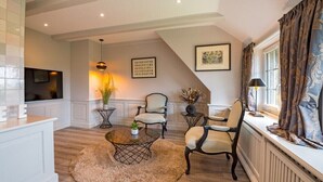 A living room with a fireplace, a television, a round coffee table, and two armchairs. - Country house North Sea (Keitum)