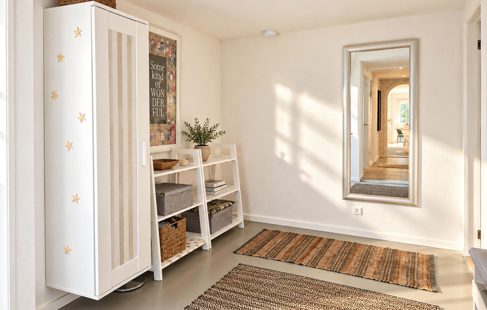 Un pasillo con un armario blanco decorado con estrellas, una estantería con libros y cestas, una planta en maceta y un espejo en la pared.