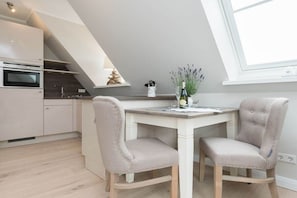 Een moderne keuken met een eethoek, met een witte tafel en stoelen, een inbouwoven en een dakraam.