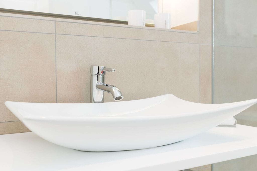 A modern bathroom with a white vessel sink, chrome faucet, and a mirror above the sink.