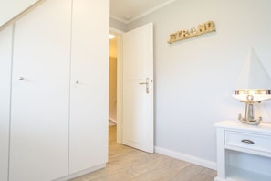 A hallway with a closed door, a white bedside table with a lamp, and a wall-mounted sign that reads 'STRAND'. - Holiday home in Kampen with swimming pool (Kampen)