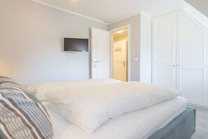 A bedroom with a bed, a television mounted on the wall, and a wardrobe. - Holiday home in Kampen with swimming pool (Kampen)